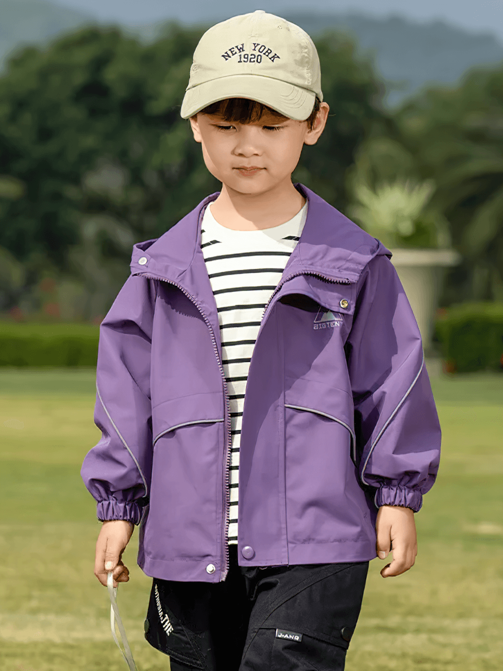 Child wearing Outdoor Waterproof Children's Windbreaker Jacket - SF3571, purple color, in a park setting with a cap on.